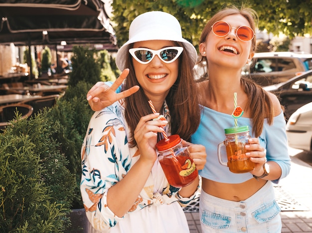 Two young beautiful smiling hipster girls in trendy summer clothes and panama hat