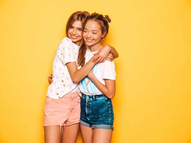 유행 여름 옷을 입고 두 젊은 아름 다운 웃는 hipster 여자. 노란 벽 근처 포즈 섹시 평온한 여자입니다. 미쳐 가고 재미있는 긍정적 인 모델.