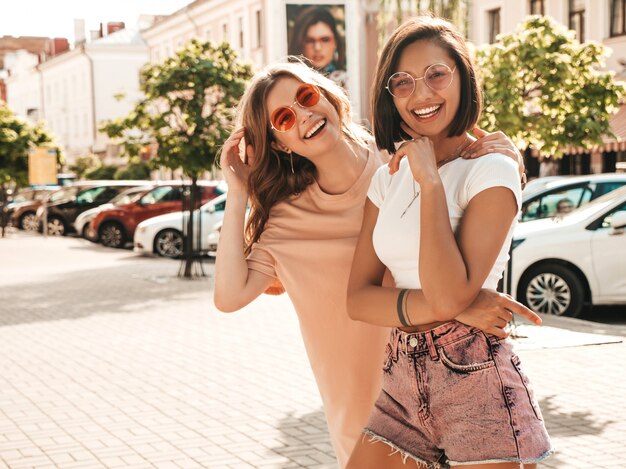 유행 여름 옷에 두 젊은 아름 다운 웃는 hipster 여자. 선글라스에 거리 배경에 포즈 섹시 평온한 여자. 재미 있고 미쳐가는 긍정적 인 모델
