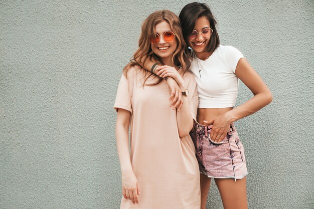 유행 여름 옷에 두 젊은 아름 다운 웃는 hipster 여자. 선글라스에 거리 배경에 포즈 섹시 평온한 여자. 재미와 포옹을 가진 긍정적 인 모델