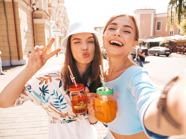 Две молодые красивые улыбающиеся хипстерские девушки в модной летней одежде