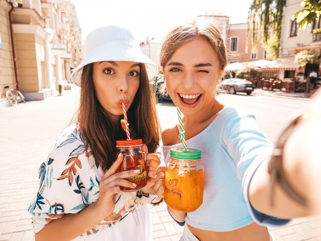 Two young beautiful smiling hipster girls in trendy summer clothes