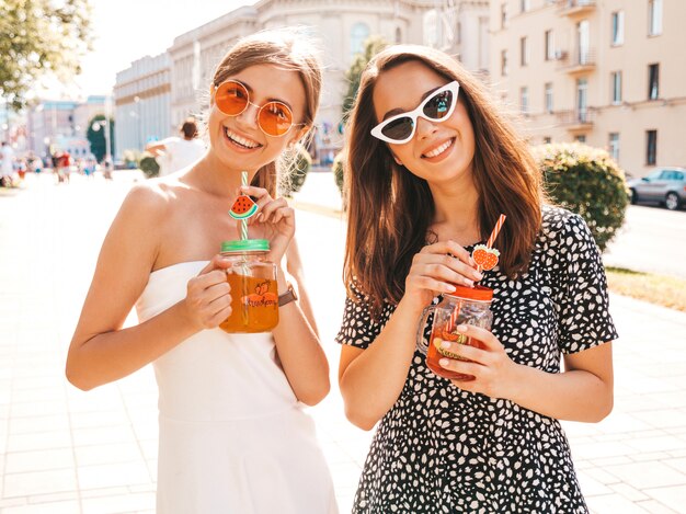 Two young beautiful smiling hipster girls in trendy summer clothes