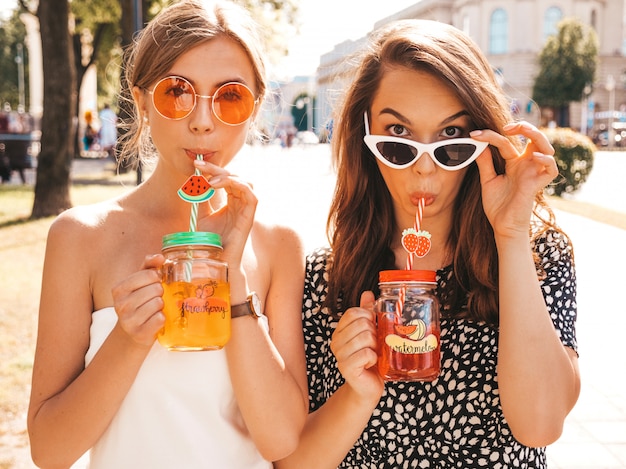 Two young beautiful smiling hipster girls in trendy summer clothes