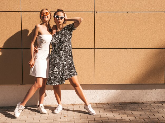 Two young beautiful smiling hipster girls in trendy summer dresses.