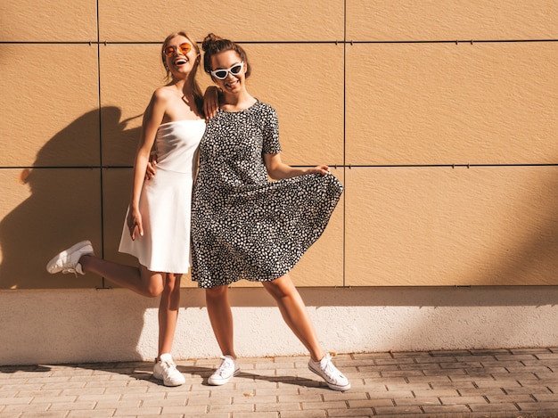 Две молодые красивые улыбающиеся битник девушки в модных летних платьях.