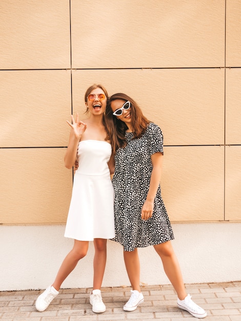 Two young beautiful smiling hipster girls in trendy summer dresses. 