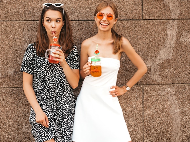 Two young beautiful smiling hipster girls in trendy summer dresses.