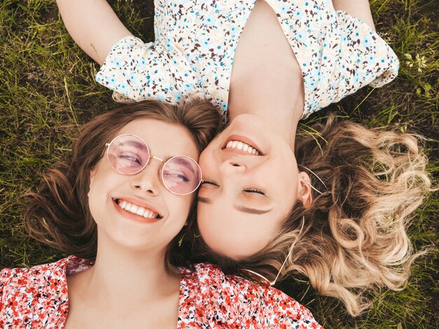 유행 여름 sundress에 두 젊은 아름 다운 웃는 hipster 여자. 선글라스에 푸른 잔디에 누워 섹시 평온한 여자. 재미있는 모델 재미.