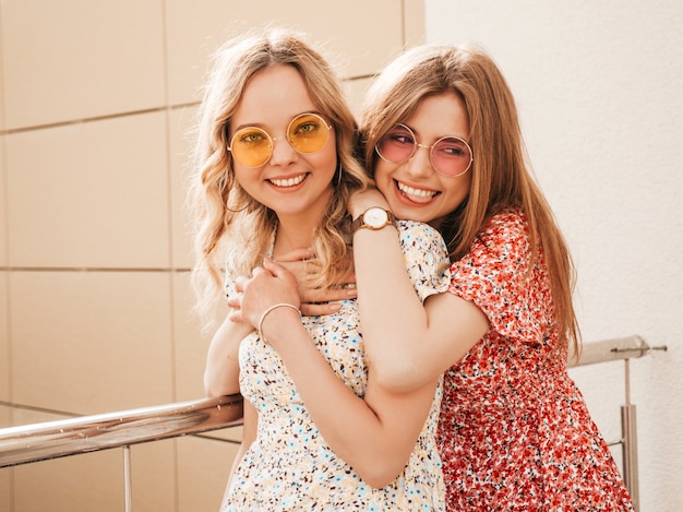 유행 여름 sundress에 두 젊은 아름 다운 웃는 hipster 여자. 모자에 거리 배경에 포즈 섹시 평온한 여자. 재미 있고 포옹하는 긍정적 인 모델.