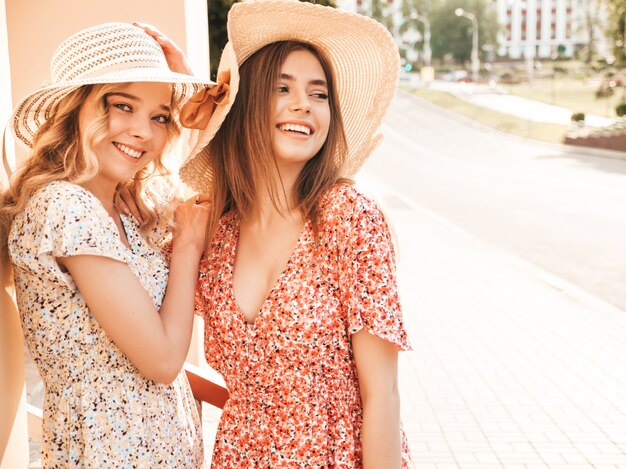 유행 여름 sundress에 두 젊은 아름 다운 웃는 hipster 여자. 모자에 거리 배경에 포즈 섹시 평온한 여자. 재미와 포옹을 가진 긍정적 인 모델