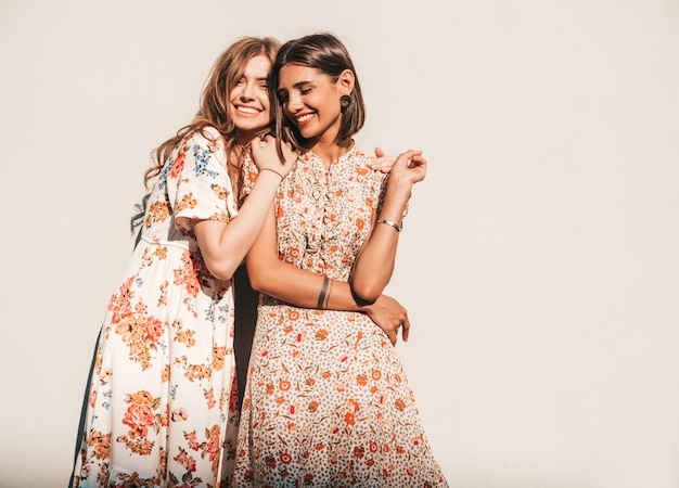 Two young beautiful smiling hipster girls in trendy summer sundresses