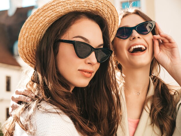 Two young beautiful smiling hipster girls in trendy white sweater and coat