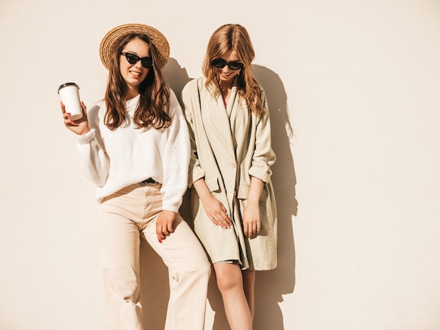 Two young beautiful smiling hipster girls in trendy white sweater and coat