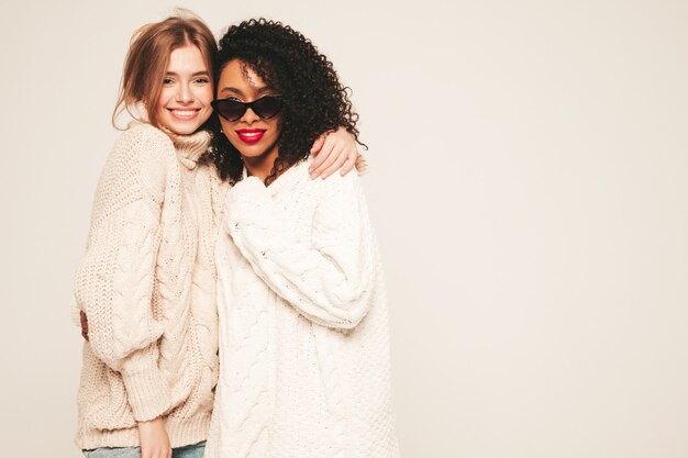 Две молодые красивые улыбающиеся хипстерские девушки в модных зимних свитерах. Позитивные модели веселятся и обнимаются