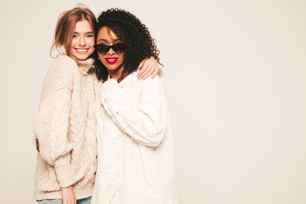 Two young beautiful smiling hipster girls in trendy winter sweaters. Positive models having fun and hugging