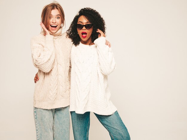 트렌디한 겨울 스웨터에 두 젊은 아름 다운 웃는 힙스터 소녀. 재미와 포옹을 하는 긍정적인 모델