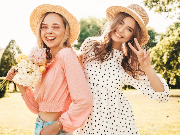 Foto gratuita due giovani bella donna sorridente hipster in prendisole estive alla moda. donne spensierate sexy che posano nel parco in cappelli.