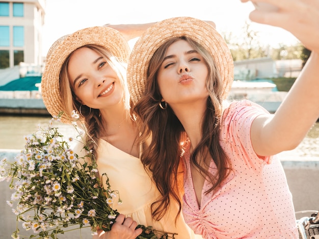 Two young beautiful smiling hipster woman in trendy summer sundress