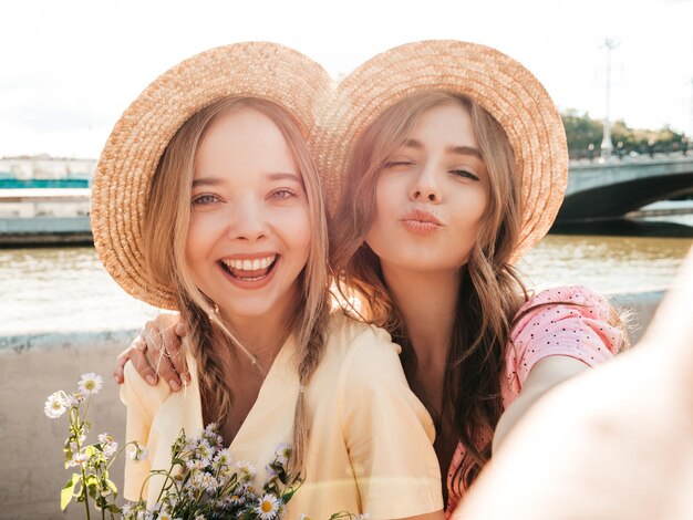 Two young beautiful smiling hipster woman in trendy summer sundress