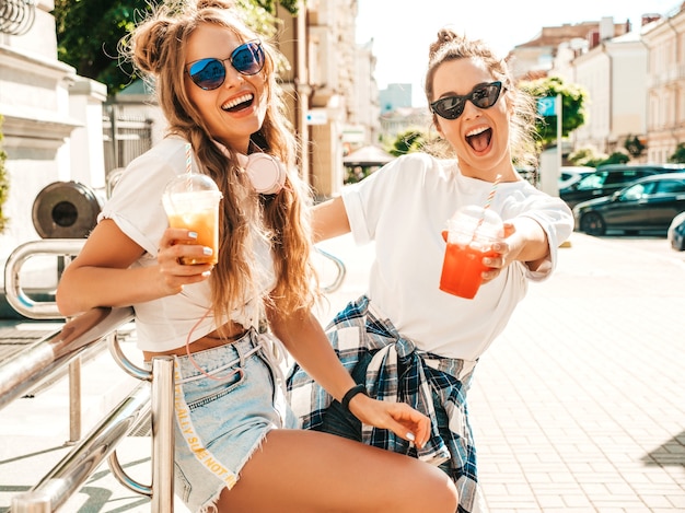 Two young beautiful smiling hipster women in trendy summer clothes