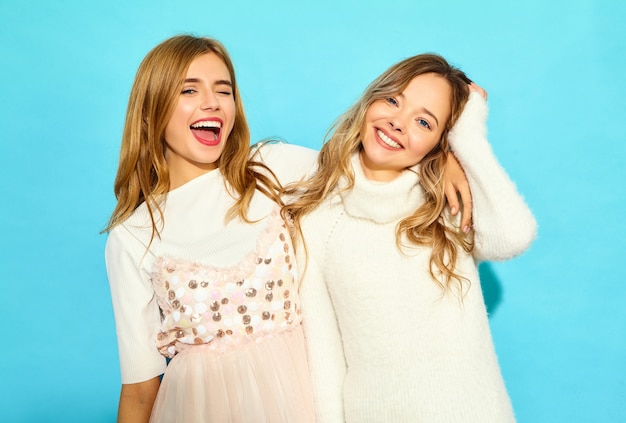 Two young beautiful smiling hipster women in trendy summer white clothes. Sexy carefree women posing near blue wall. Positive models