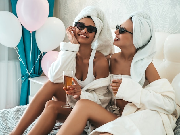 Two young beautiful smiling women in white bathrobes and towels on head