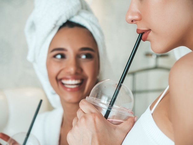 Due giovani belle donne sorridenti in accappatoi bianchi e asciugamani sulla testa