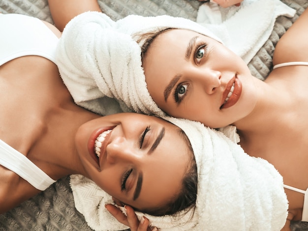 흰 목욕 가운과 머리에 수건을 입은 두 젊은 아름다운 웃는 여성
