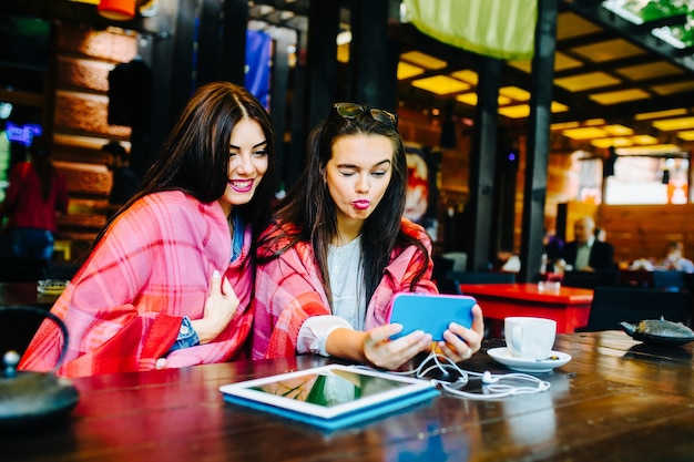 Two young and beautiful women sitting at the table and doing selfie in the cafe