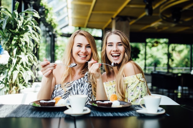 Two young, blonde sisters have a breakfast in modern cafe, spend time together