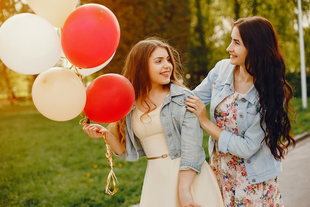 две молодые и яркие девушки проводят время в летнем парке с воздушными шарами