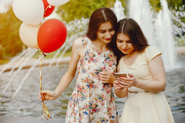две молодые и яркие девушки проводят время в летнем парке с воздушными шарами