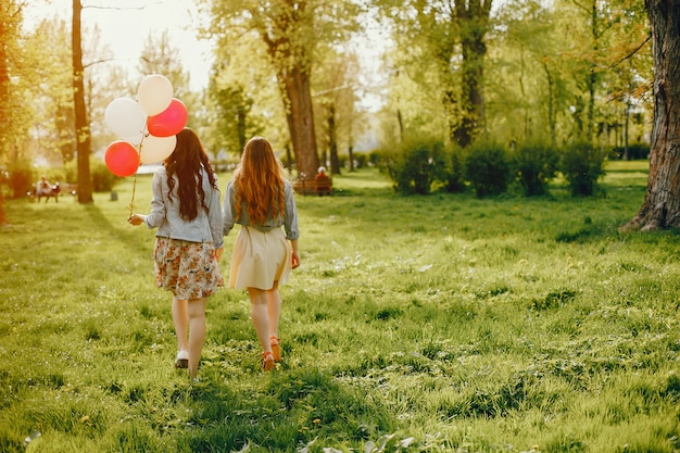 젊고 밝은 두 소녀는 여름 공원에서 풍선과 함께 시간을 보냅니다.