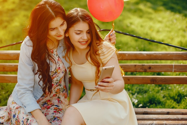 Free photo two young and bright girls spend their time in the summer park with balloons