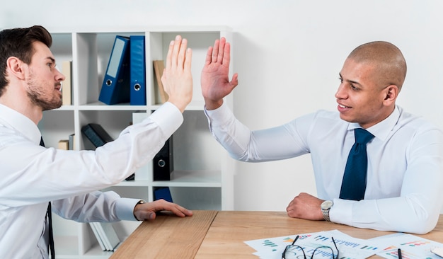 Two young businessman giving the high-five to each other at workplace