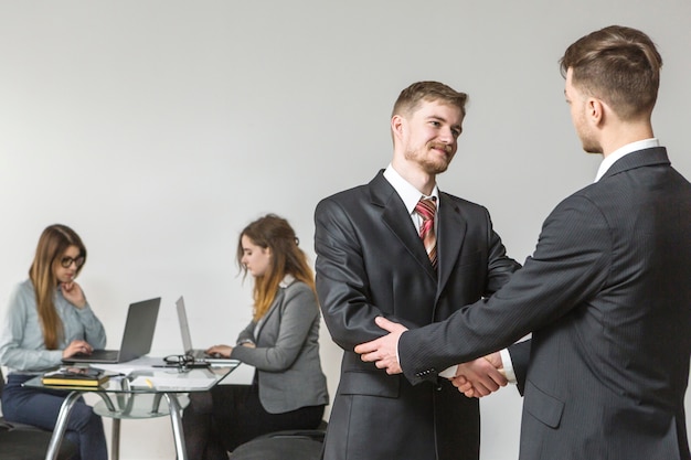 Two young businessmen shaking hands during meeting in office