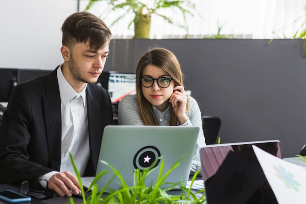 Free photo two young businesspeople using laptop at workplace