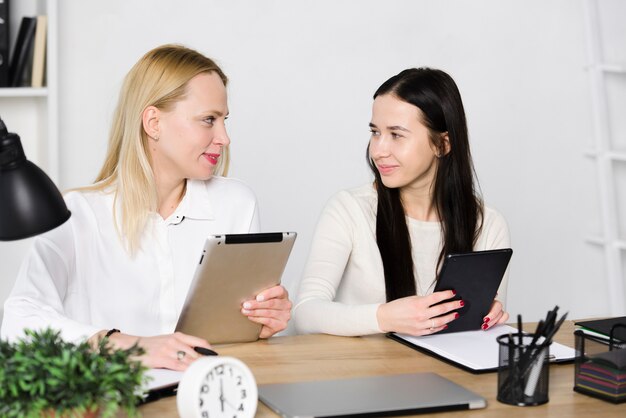 Two young businesswoman looking at each other holding digital tablet and mobile phone in hands