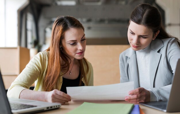 Two young businesswoman looking at paper in office