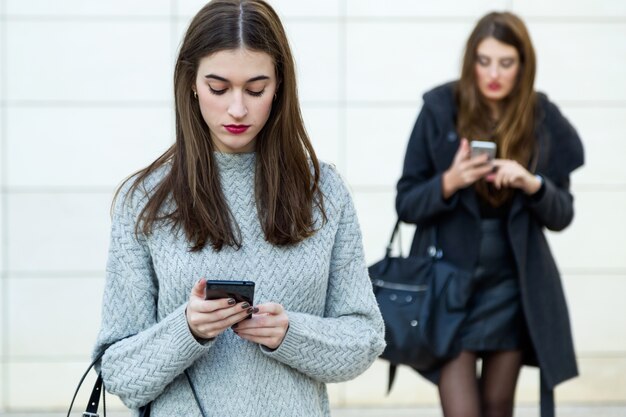 Two young businesswoman using mobile phone in the street.