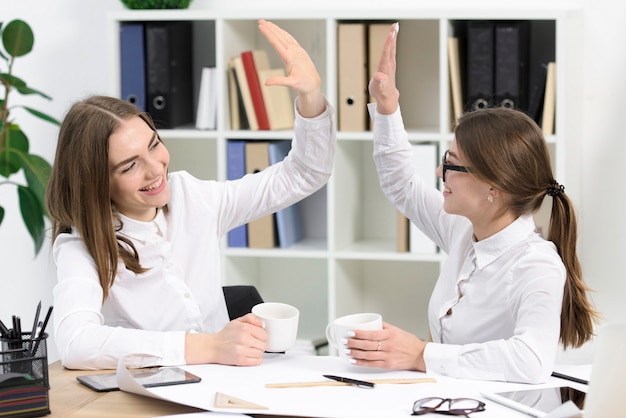 Two young businesswomen looking at each other giving high five to each other in the office