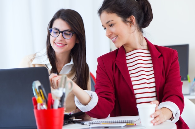 Two young businesswomen working with laptop in her office.