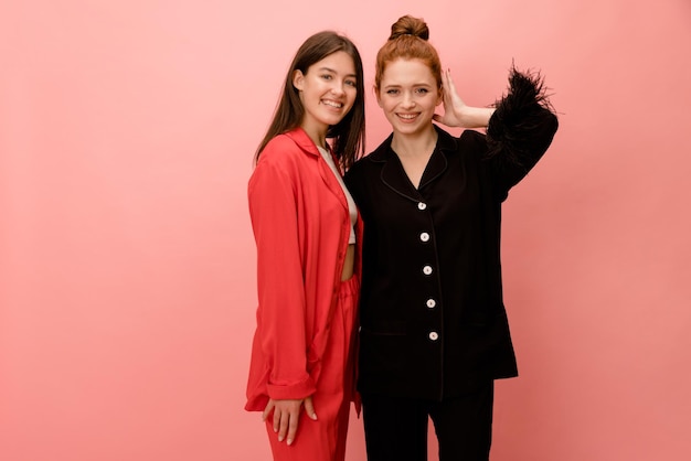 Two young caucasian girlfriends brunette and redhead in studio wear natural organic silk pant shirt suit Luxury lifestyle