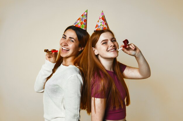 Two young caucasian girls in birthday hats are sincerely smiling