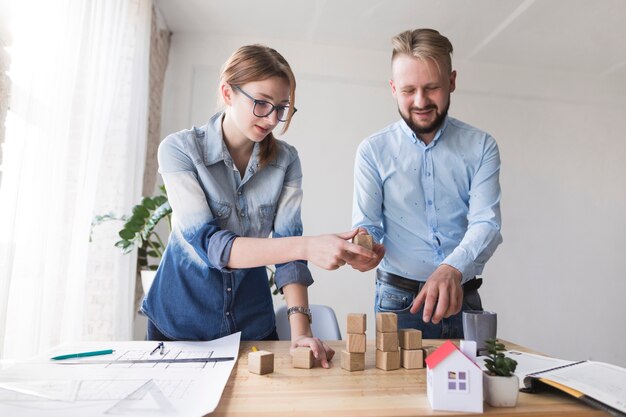 Two young colleagues stacking wooden block on business desk