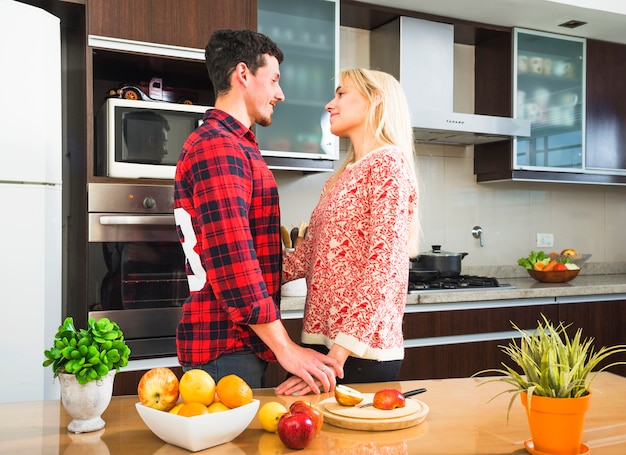 Free photo two young couple standing behind the table with fruits looking at each other