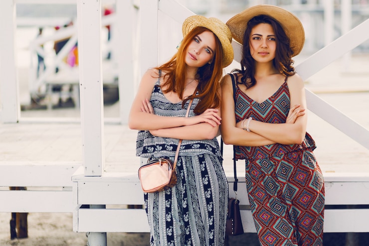 Free Photo two young fashionable women in straw hat and stylish summer outfit posing near tropical beach bar