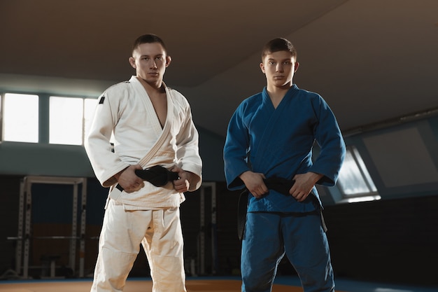 Два молодых бойца в кимоно тренируют боевые искусства в спортзале