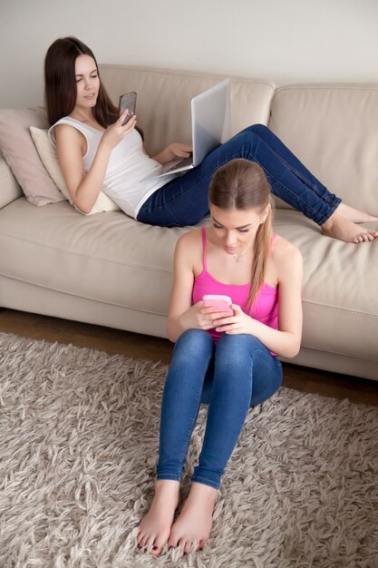 두 젊은 여자 친구 집에서 편안 하 고 스마트 폰을 사용 하여.